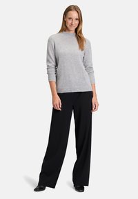 Világosszürke, kerek nyakú pulóver hosszú ujjal, fekete, bő szárú nadrággal párosítva. Sima textúra és minimalista dizájn. Fekete lábbeli.