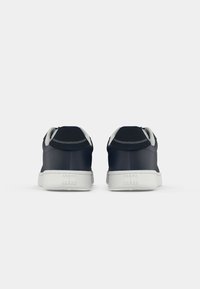 Baskets en cuir marine avec une semelle en caoutchouc blanche, un col rembourré et des accents de couture au niveau du talon, vues de l'arrière.