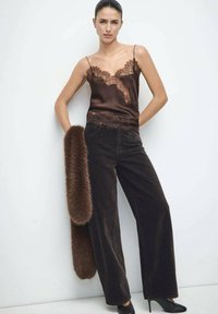 Camisola de satén marrón con encaje, combinada con pantalones de pana de pierna ancha oscuros y una larga estola marrón de piel sintética. Zapatos negros de tacón alto.