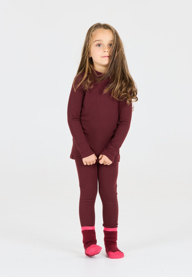 Bordeaux lange mouwen top en legging, gemaakt van zachte stof. Roze en kastanjebruine sokken met manchetaccenten. Kind staat, handen samengevouwen.
