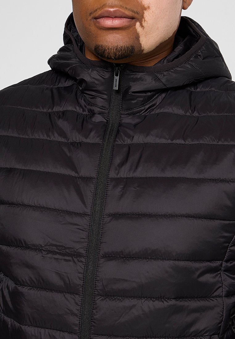 Giacca nera imbottita con chiusura a zip frontale e cappuccio. Presenta cuciture orizzontali per texture e una finitura leggera e lucida.