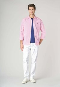 Camicia a righe rosa e bianche con bottoni da uomo, t-shirt blu navy sotto, pantaloni bianchi e sneakers bianche; vestibilità casual, maniche lunghe.