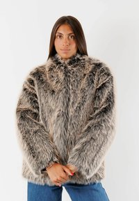 Cappotto in pelliccia sintetica nei toni del marrone chiaro e grigio, con colletto alto e vestibilità ampia. Texture morbida con maniche lunghe, mostrato con le mani unite.