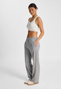 Biały sportowy biustonosz z logo, w połączeniu z luźnymi szarymi spodniami dresowymi z kieszeniami i subtelnym akcentem logo, dopełnione kremowymi trampkami.