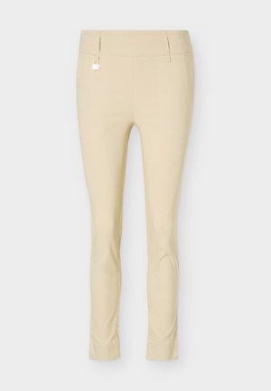 Μπεζ παντελόνι slim-fit με θηλιές για ζώνη και μικρή ασημένια λεπτομέρεια με κρίκο στην αριστερή πλευρά, εμφανιζόμενο σε απλό φόντο.