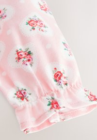 Tissu rose avec poignets élastiques présentant des formes de cœur blanches et de petits motifs floraux de roses rouges et roses.
