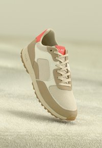 Beige and tan athletic shoe with mesh and leather materials. Features a coral red accent on the heel and neutral textured sole.