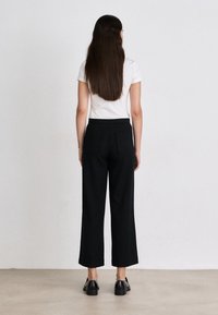 Black wide-leg trousers with a high waist, two back pockets, paired with a white short-sleeve shirt, shown from the back.