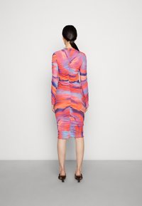 Långärmad figursydd klänning med livfulla mönster i orange, rosa och blåa svall, med rynkdetaljer och knälig längd.