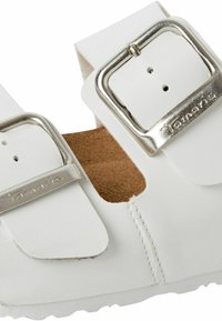 White sandals with two adjustable metallic buckles, soft inner lining, textured footbed, and durable sole. Simple, functional design.