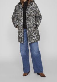 Abrigo tipo puff con un patrón de estampado de leopardo, en colores negro y beige, que cuenta con capucha y cierre de cremallera, combinado con unos vaqueros de pierna ancha en un tono azul claro.