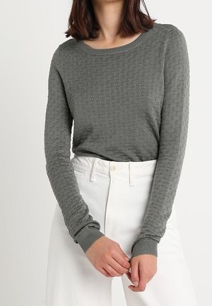 Maglione grigio texturizzato a maniche lunghe con scollo rotondo e polsini a costine, abbinato a pantaloni bianchi a vita alta.