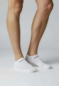 Weiße Knöchelsocken mit dem Schriftzug "SIXTH" in schwarzem, strukturiertem Stoff, enger Passform und flachem Schnitt, getragen an schlanken Beinen.