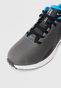 Pilkos ir juodos Nike bėgimo bateliai su juodais raišteliais, mėlynu pamušalu ir mažuoju mėlynu Nike swoosh ant pirštų srities.