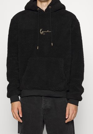 Sudadera con capucha de forro polar negra con superficie texturizada, capucha con cordón y logo bordado en dorado. Presenta un bolsillo frontal y puños acanalados.