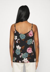 Květinový top bez rukávů s velkými růžovými a modrými květinami na černém pozadí. Tenké ramínka a volný, lehký design ze tkaniny.