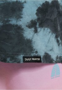 Lühikese varrukaga t-särk sinise ja halli batikmustriga, millel on must silt "JUST RHYSE" ja kerge sinine lehekujundus all.