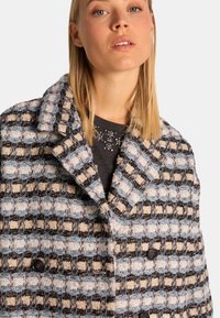Abrigo de doble botonadura con un patrón tejido en azul, crema y negro. Cuenta con solapas con muescas y dos botones negros. Tejido texturizado.