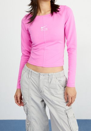 Kvinde iført en tætsiddende lyserød cropped langærmet top med hvidt Nike Air-logo og lysegrå cargobukser med lommer.