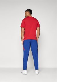 Camiseta de algodón roja combinada con pantalones deportivos azules con acentos rojos, un ajuste entallado y detalles de franjas blancas cerca de los tobillos.