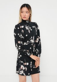 Vestido preto com padrão floral, mangas longas e bufantes e decote alto. Apresenta um cinto amarrado e padrões de flores brancas e rosas por todo o vestido.