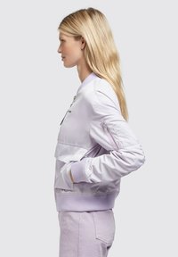 Heled lilla bomber-jakk, millel on soonilised varrukad, lukuga taskud ja kihiline esikujundus. Sile kangas, millel on kerge sära.