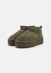 Olive green suede ankle boots with a rounded toe and flat platform sole. Features a contrasting stitched trim and a pull tab at the back.