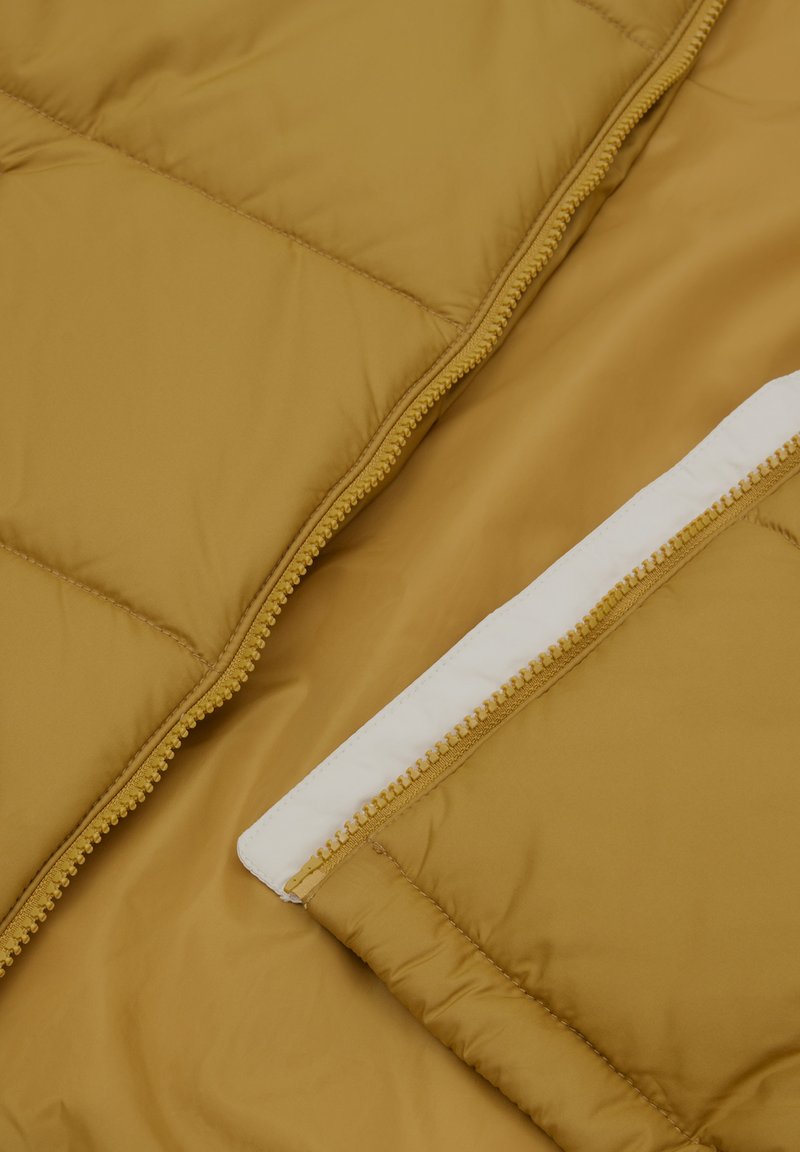 Intérieur d'une veste rembourrée jaune avec une poche zippée blanche contrastante, texture lisse et motif matelassé pour l'isolation.