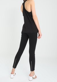 Svart ärmlös topp med racerback-design, i kombination med svarta smala byxor med dragkedjor vid ankeln. Modellen bär vita klackar.