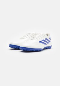 Scarpe da calcio bianche con accenti blu, dotate di una parte superiore in sintetico liscio, suola testurizzata e tre strisce blu lungo il lato.