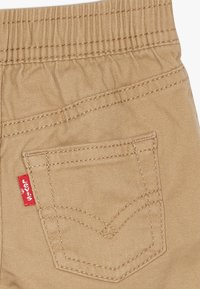 Beżowe bawełniane spodnie z elastycznym paskiem, z tylną kieszenią z czerwoną metką Levi's i kontrastującymi detalami szwów.