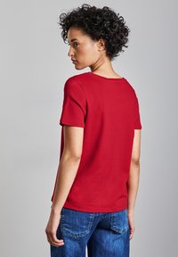 Rode t-shirt met korte mouwen en een ronde halslijn, gemaakt van een soepele stof, gedragen met blauwe spijkerbroek. De pasvorm is relaxed en casual.