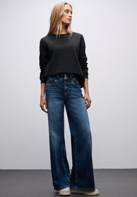 Jeans a gamba larga in denim blu con una texture lavata, abbinati a un maglione nero attillato. Design semplice e casual con accenti minimalisti.