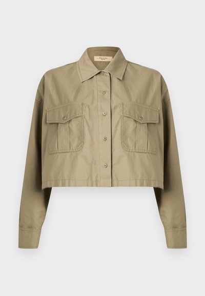 Περικομμένο χακί πουκάμισο με μακριά μανίκια, κουμπιά, μυτερό γιακά και δύο τσεπάκια στο στήθος με κουμπιά.