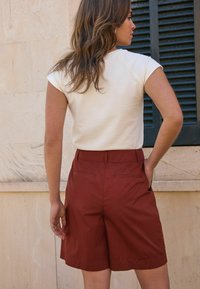 Haut crème à manches courtes associé à un short taille haute de couleur rouille. Le short présente un design plissé et des poches arrière. Tissu texturé.