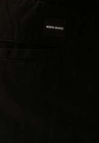 Svart tyg med en slät textur, med en sydd ficka och en rektangulär etikett som säger "MODERN ARCHIVES" i vit text.