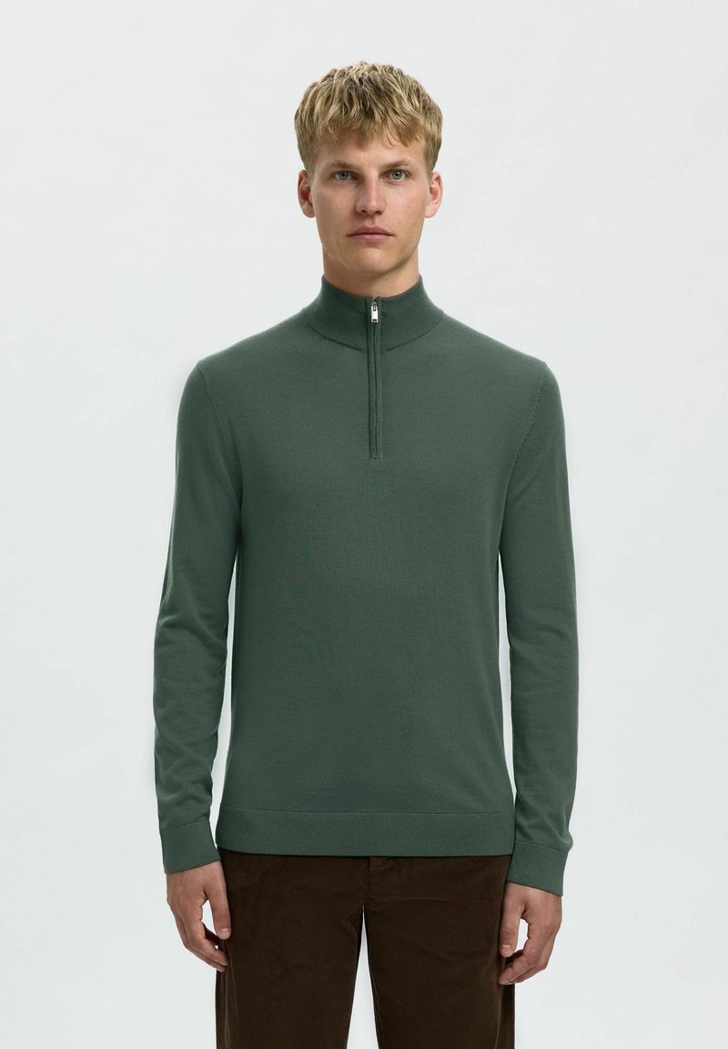 Grüner Strickpullover mit hohem Kragen und halb zip. Verfügt über lange Ärmel und eine glatte Textur. Kombiniert mit braunen Cordhosen.
