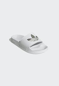 White slide sandal with textured strap, featuring a cut-out Adidas logo. Smooth footbed and rubber sole, designed for casual wear.