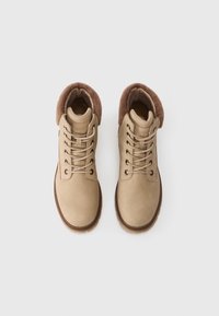 Bottes chelsea beiges avec un dessus en cuir lisse, un design à lacets, un col en fausse fourrure marron et des détails de semelle marron contrastants.