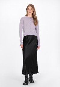 Cardigan lung cu maneci lungi din lavandă, cu nasturi, peste o fustă midi din satin negru, asortată cu botine negre până la gleznă. Texturi netede și culori contrastante.