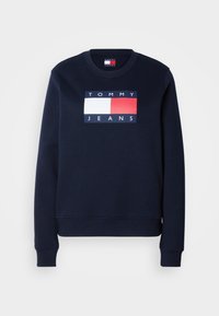 Sweat-shirt bleu marine col rond avec poignets et ourlet côtelés, présentant un logo rectangulaire Tommy Jeans avec des blocs de couleur blanc, rouge et bleu marine sur la poitrine.