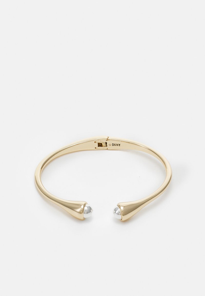 Bracciale a manica in tono dorato con due estremità affusolate e dettagli in perline tono argento. Finitura metallica liscia e lucida con un design elegante e moderno.