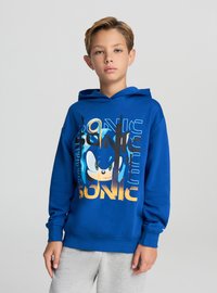 Felpa con cappuccio blu con grafica di Sonic the Hedgehog, testo giallo e vestibilità comoda, realizzata in morbido cotone. Pantaloni grigi.