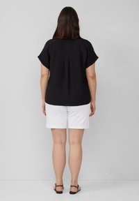 Zwarte blouse met korte mouwen en een losse pasvorm, van een gestructureerde stof, met een plooitje aan de achterkant, gecombineerd met witte shorts met omgeslagen zoom en zwarte sandalen.