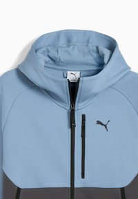 Lys blå zip-up hoodie med et sort Puma-logo på brystet og to frontlommer med lynlås, lavet af blødt stof og med hætte.