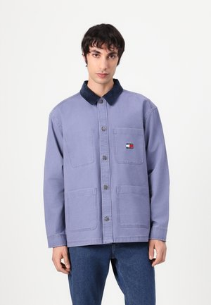 Veste violette en coton avec un col en velours côtelé bleu marine, comportant deux poches avant et un petit patch logo sur la poitrine.
