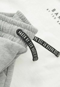 Grauer Baumwollzugbund mit gerippter Textur, mit einem schwarzen Etikett mit der Aufschrift "BAKER by TED BAKER" auf weißem Hintergrund.