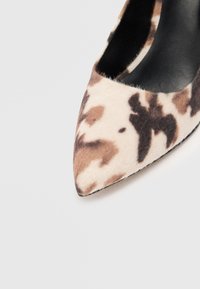 Escarpin à bout pointu en imprimé animal beige et marron, fabriqué en daim texturé avec un intérieur noir, présentant une silhouette élégante et un talon étroit.
