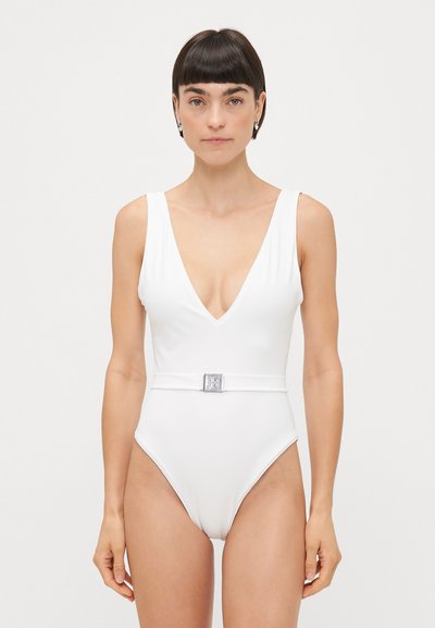 Hvid one-piece badedragt med dyb V-hals, brede stropper og en tætsiddende talje med en firkantet sølvspænde detalje. Glat tekstur.