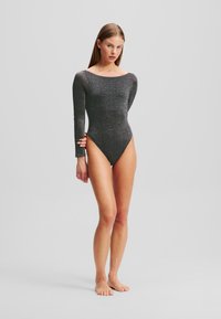 Schwarzer Langarm-Body aus schimmerndem Material, mit einem weiten Halsausschnitt und hoch geschnittenen Seiten, die eine schlanke Silhouette betonen.